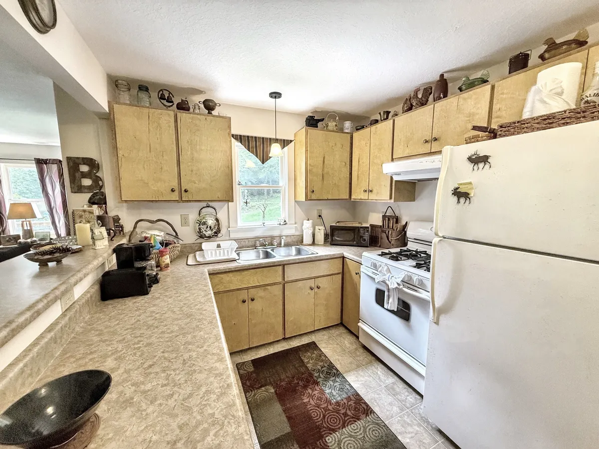 A warmly lit kitchen featuring charming cabinets, a farmhouse sink, and a stove, with decorative items neatly arranged on open shelves. The scene subtly hints at recent meal preparations, evoking a sense of home and tradition.