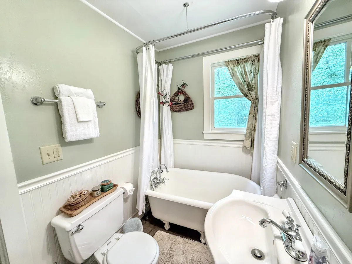 A serene bathroom with a classic clawfoot bathtub positioned by a window with sheer curtains, a stylish vanity sink, and decorative wall baskets. The space encourages relaxation and self-care rituals.