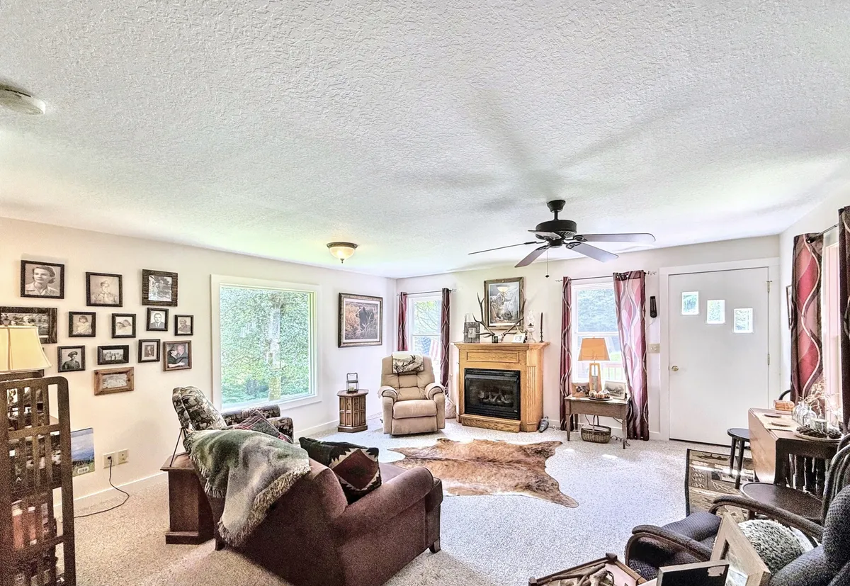 A welcoming communal living room with a cozy fireplace, large windows letting in natural light, framed photos on the wall, and comfortable seating arranged for gatherings. The space radiates warmth and is ideal for family storytelling, holiday celebrations, and quiet relaxation.