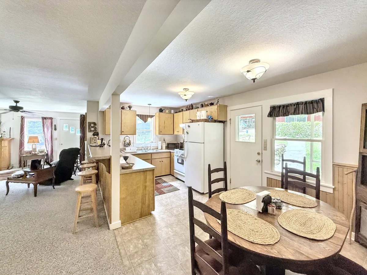 A dining table set with placemats blends into a comfortable seating area and a kitchen with warm wooden cabinets, creating a welcoming, cozy backdrop for family meals, game nights, and casual gatherings.