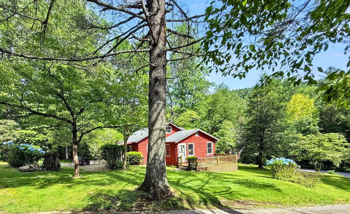 The red cottage nestled among large green trees, surrounded by a lush lawn and a welcoming wooden deck. The environment feels peaceful and rejuvenating, offering an inviting starting point or a restful return from adventures.