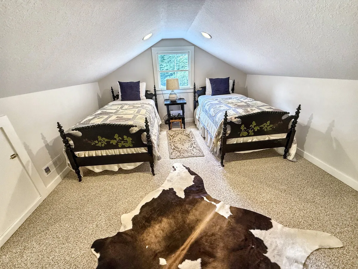 A pair of twin beds with decorative pillows and a cowhide rug form a cozy sleeping area. Soft lighting and a nightstand with a lamp set an inviting mood for bedtime stories or quiet relaxation.