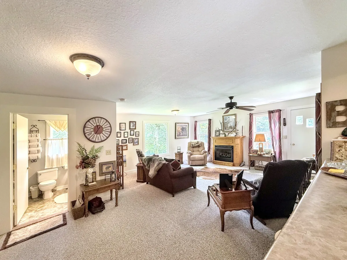 A cozy living room featuring a central gas fireplace surrounded by comfortable seating, large windows bringing in natural light, and tasteful decorative wall art. The arrangement encourages gathering and conversation, with the warmth of the fireplace as a clear focal point.